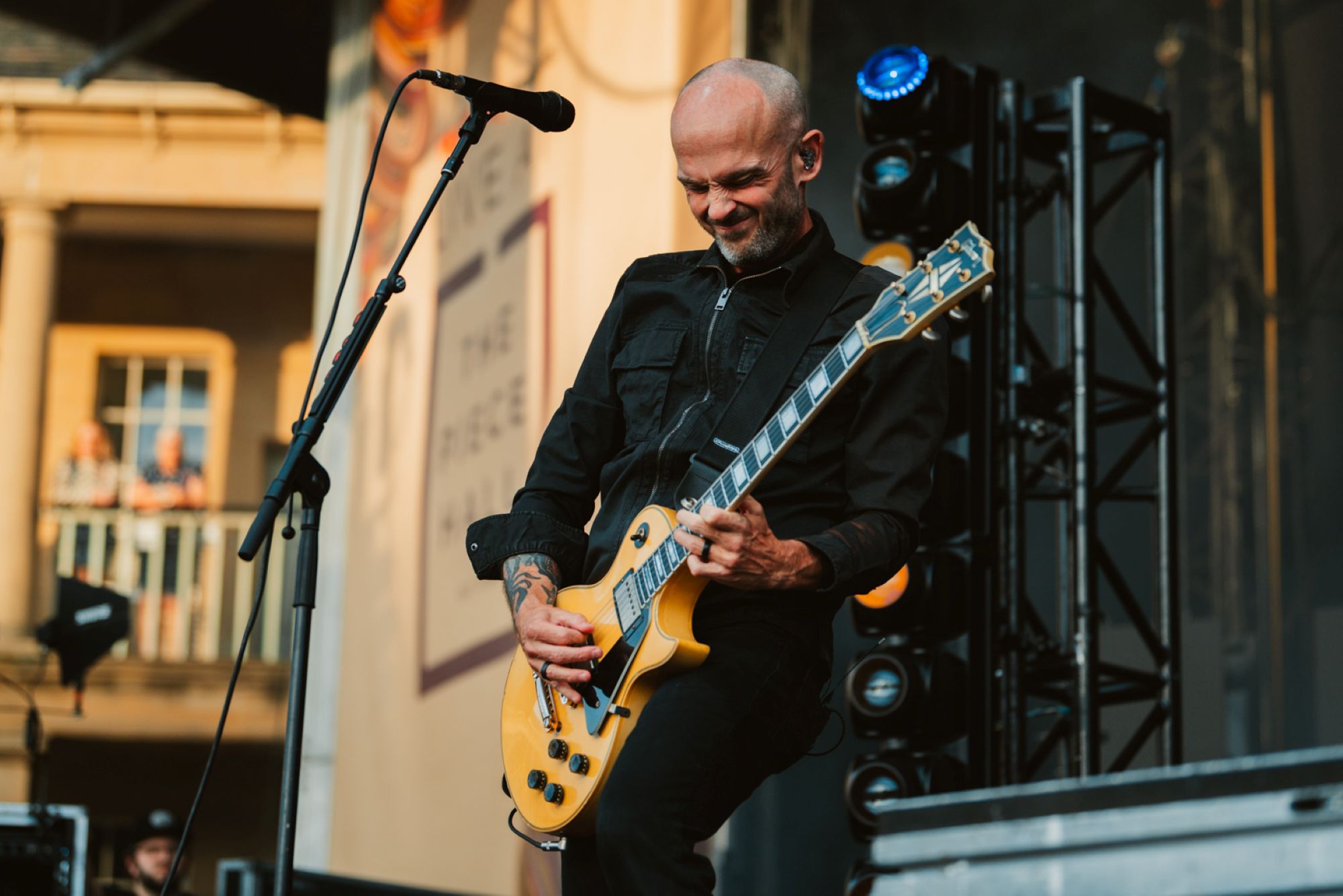 Musician playing electric guitar on outdoor stage with columns
