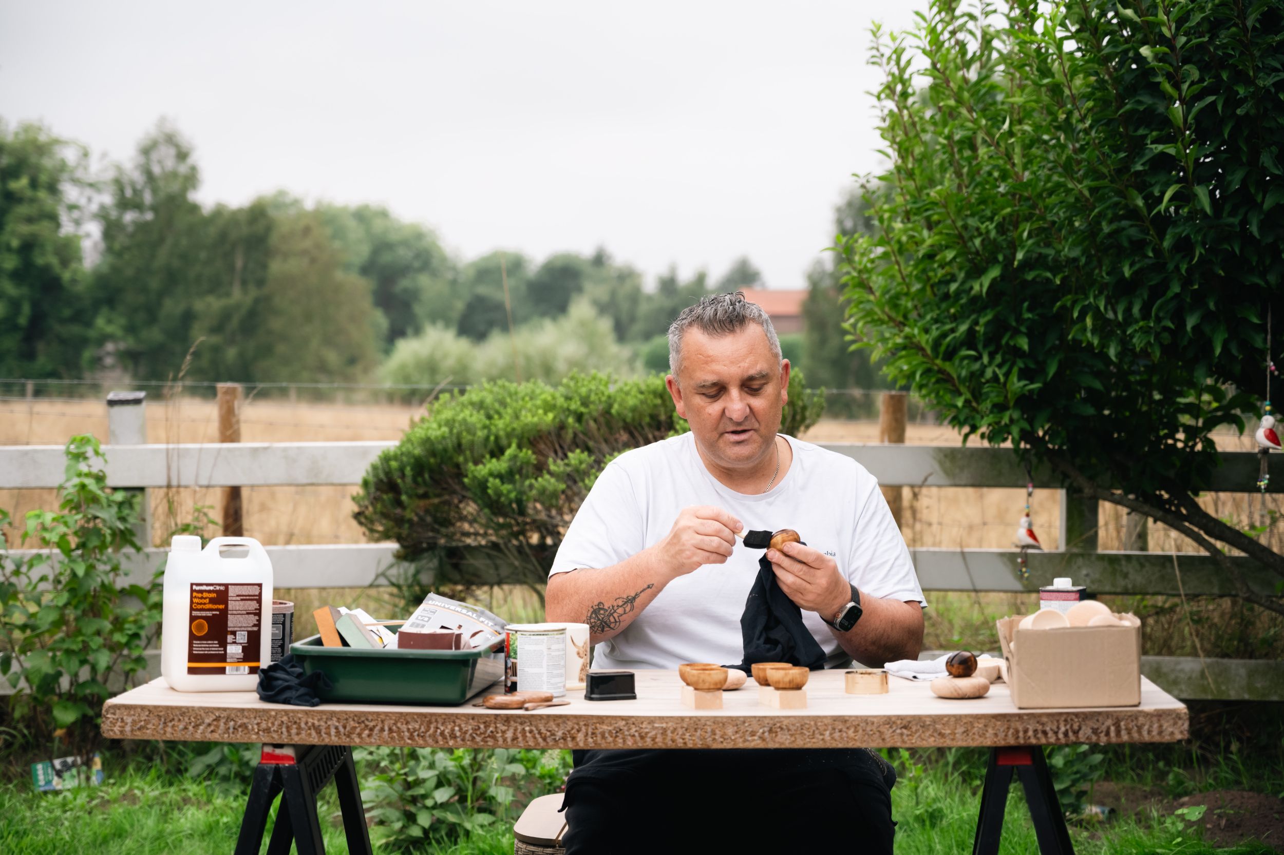 Man polishing wooden bowls at outdoor table in countryside
