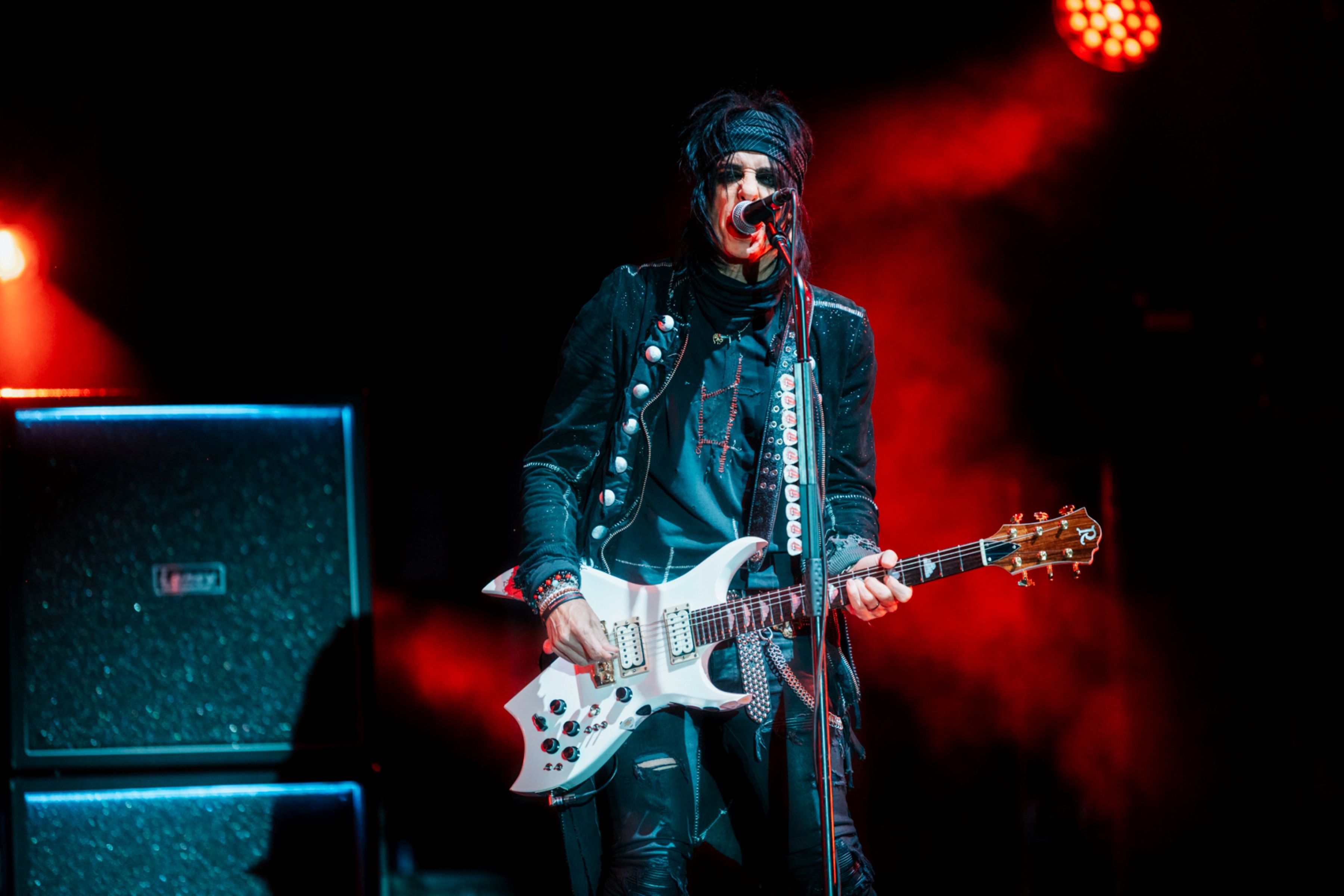 Guitarist in black outfit performing on stage with red lighting