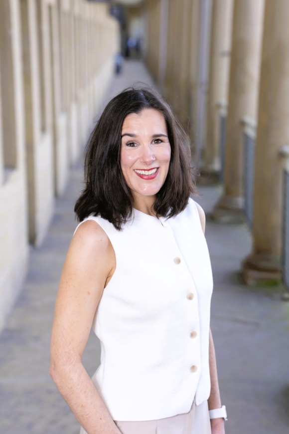 Smiling woman in white top standing in historic columned walkway
