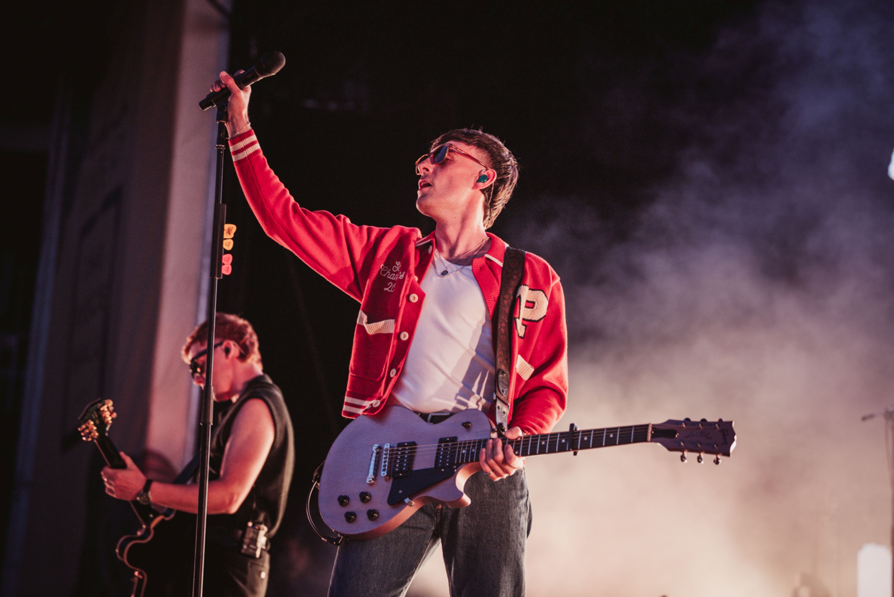 Musician in red jacket playing guitar on stage with smoke effects