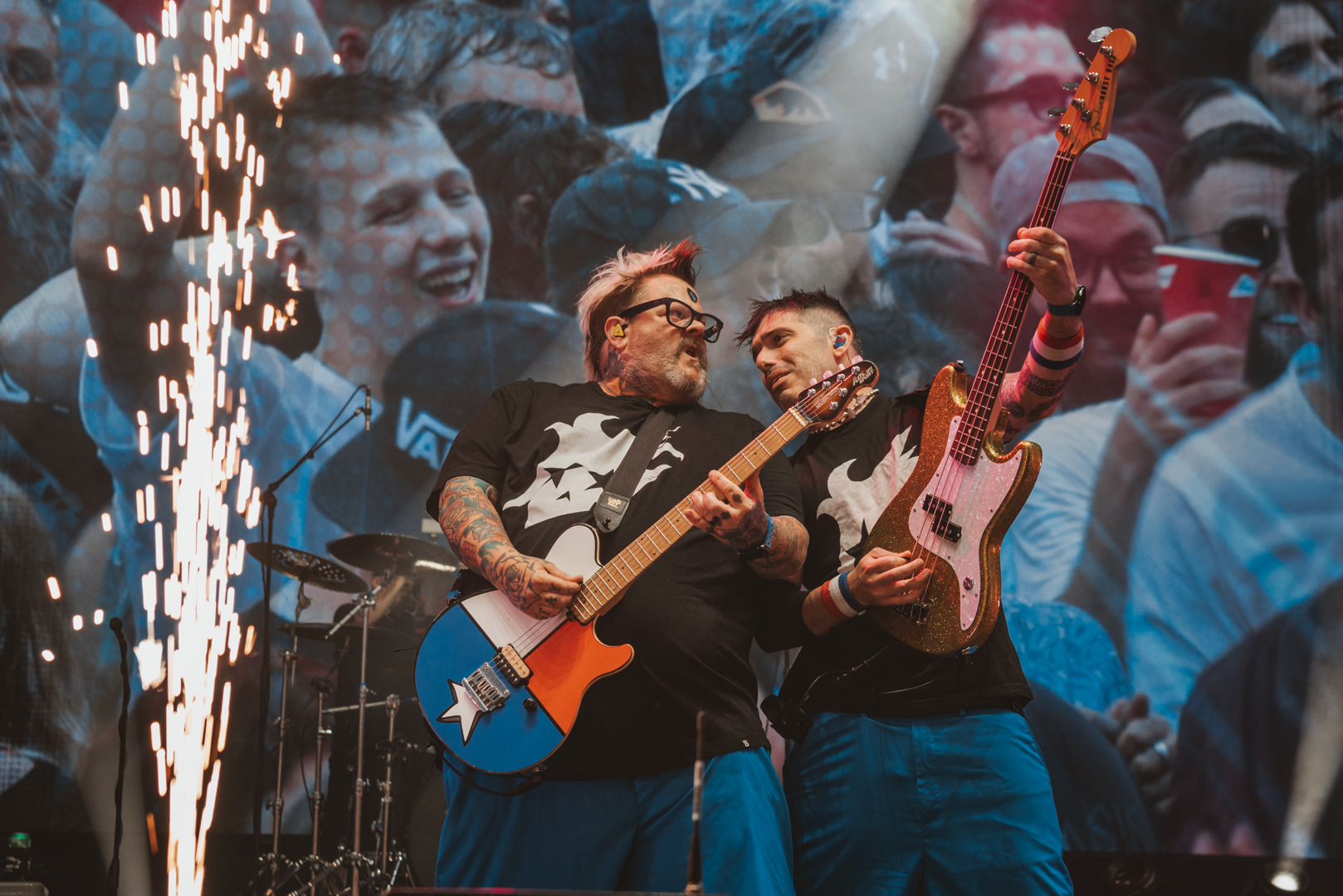 Two musicians playing guitars on stage with cheering crowd