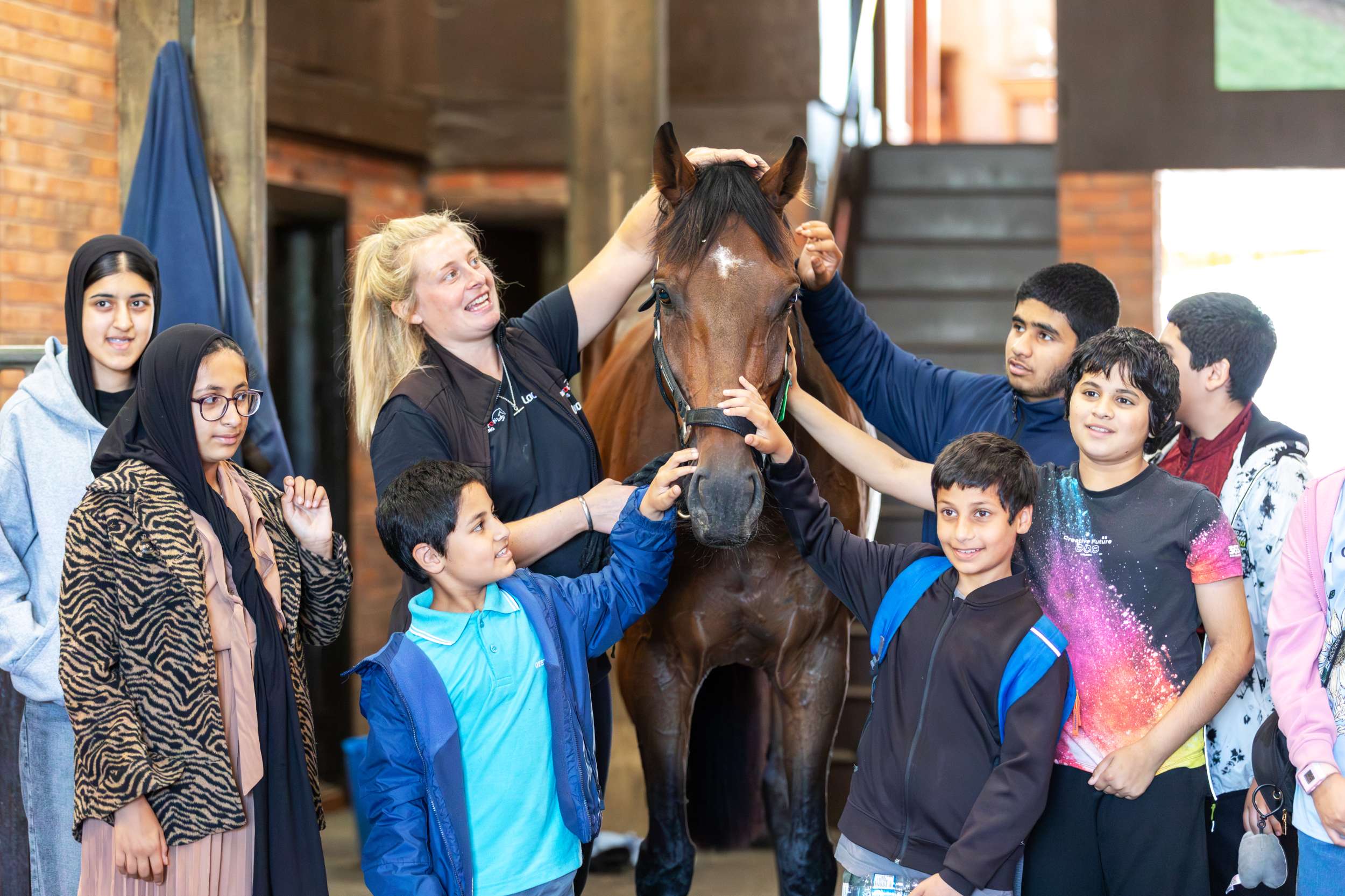 Group of children petting a horse in a stable with a trainer