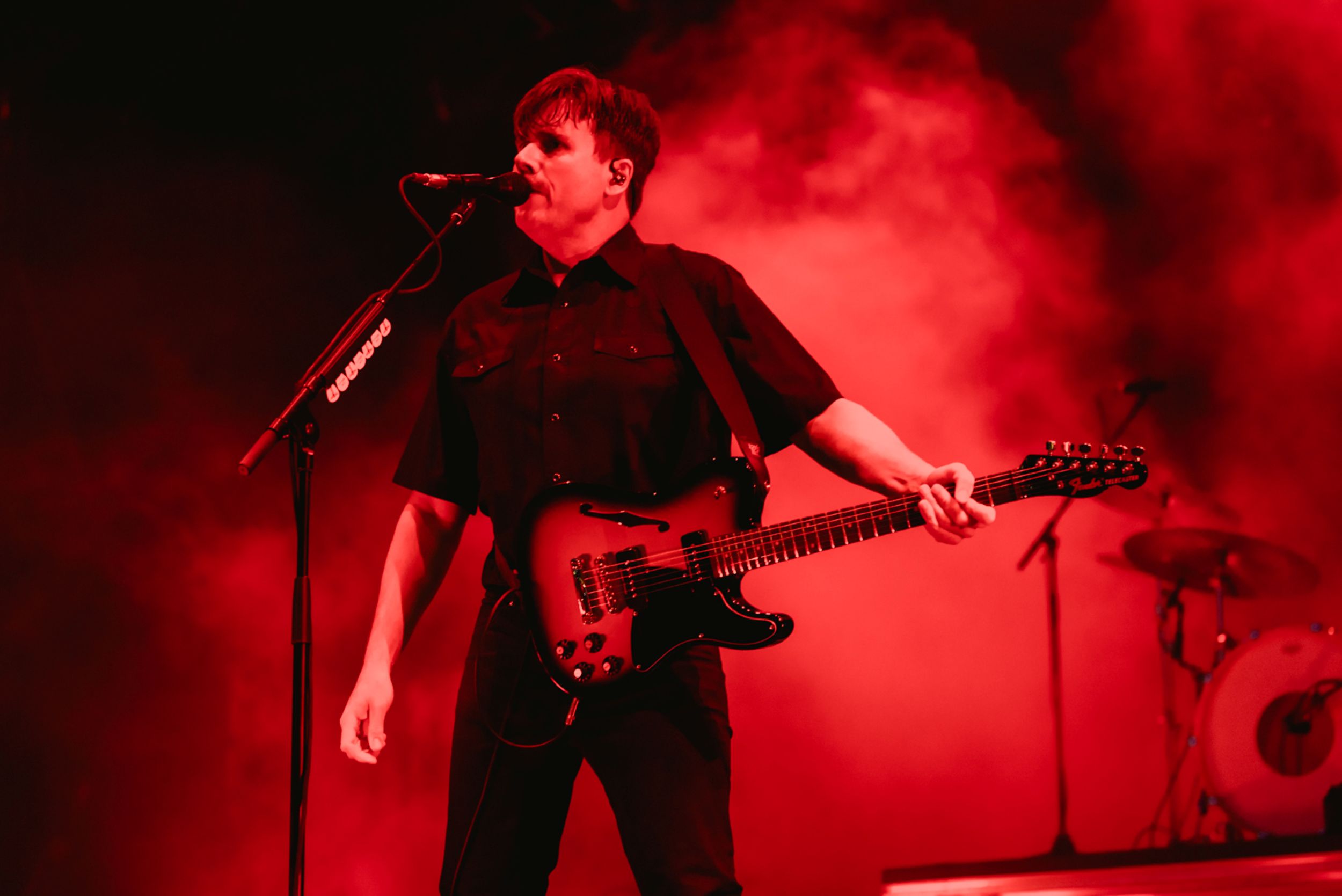 Musician in black shirt performing on stage with red lighting