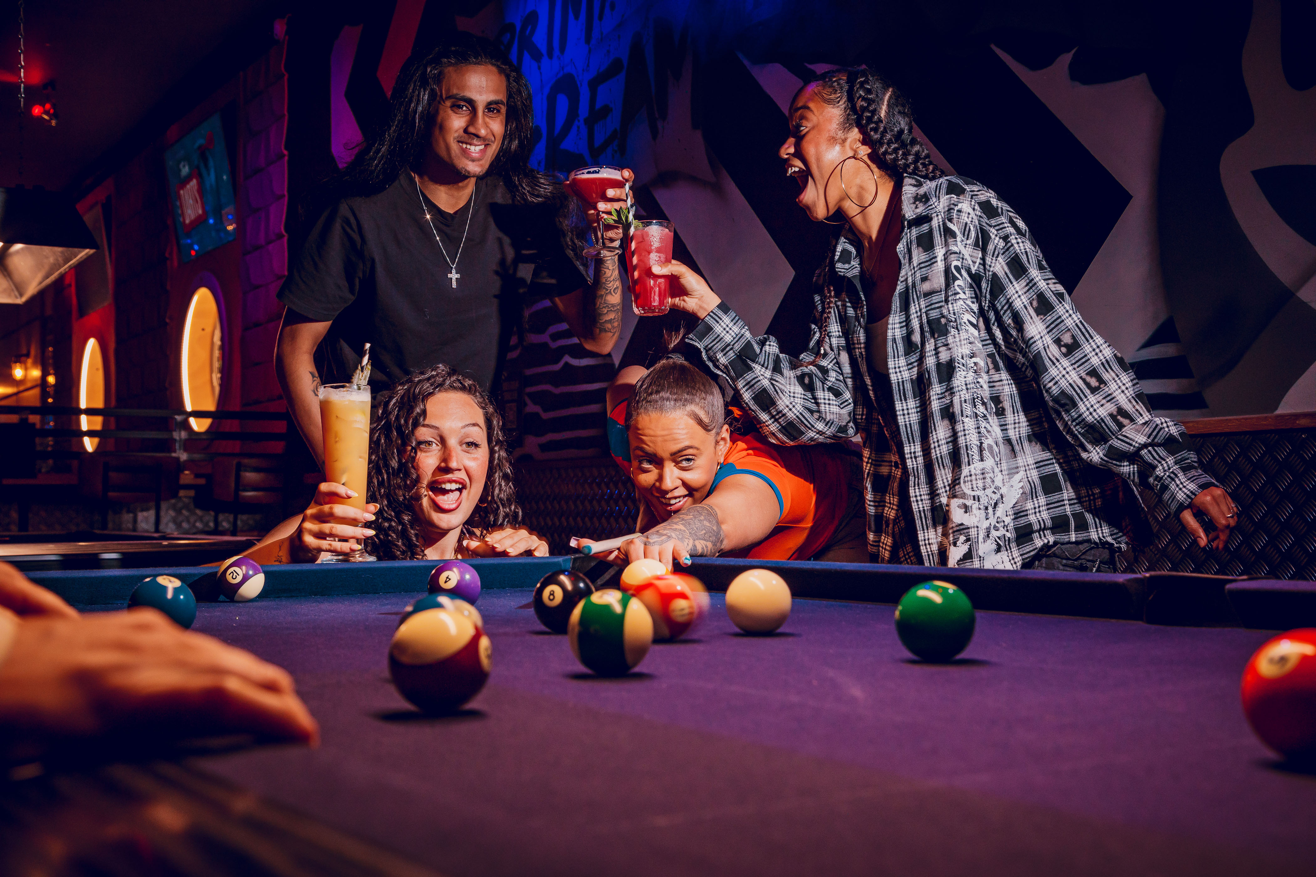 Group of friends laughing and playing pool indoors