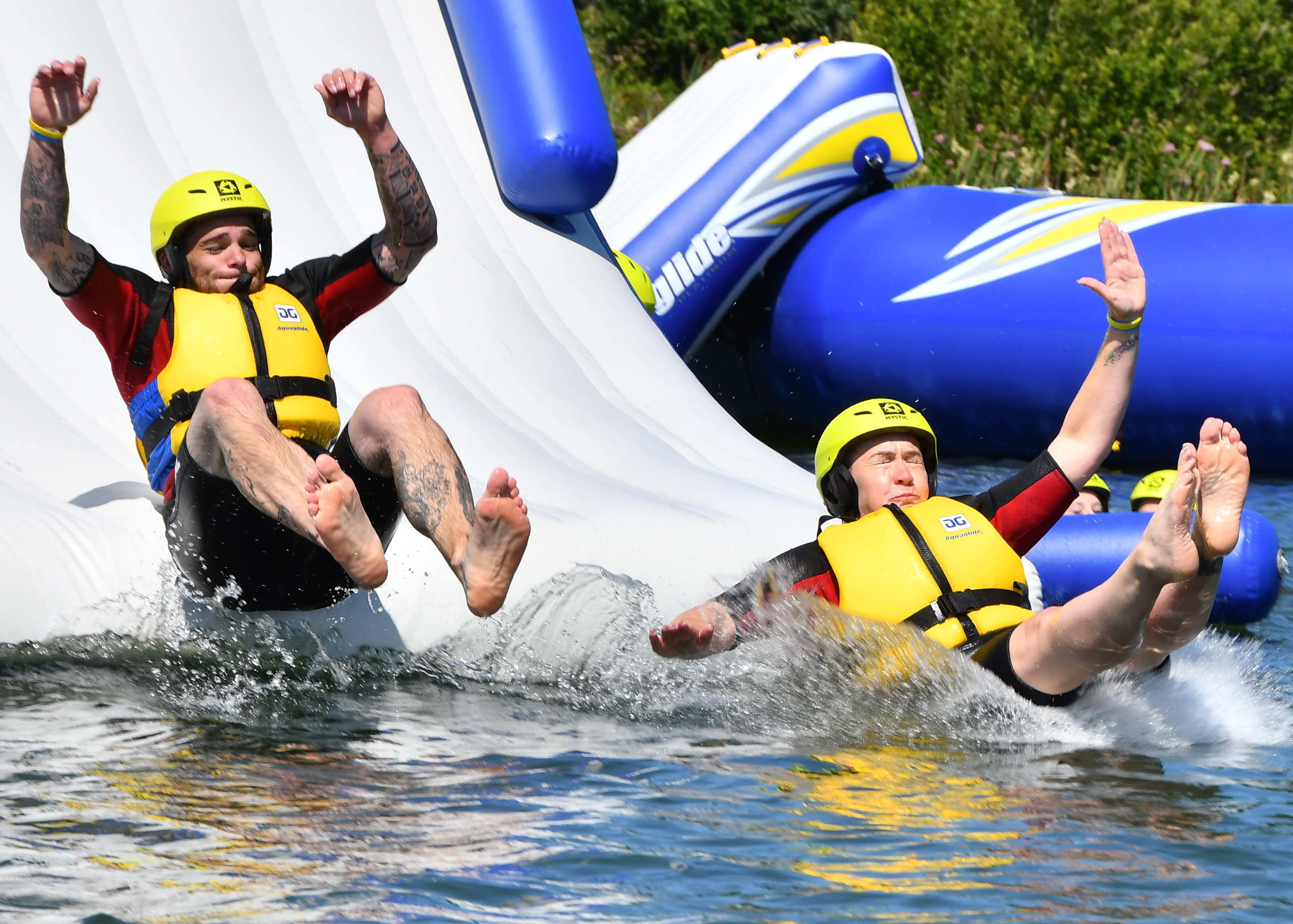 Two people in yellow life jackets sliding into a lake