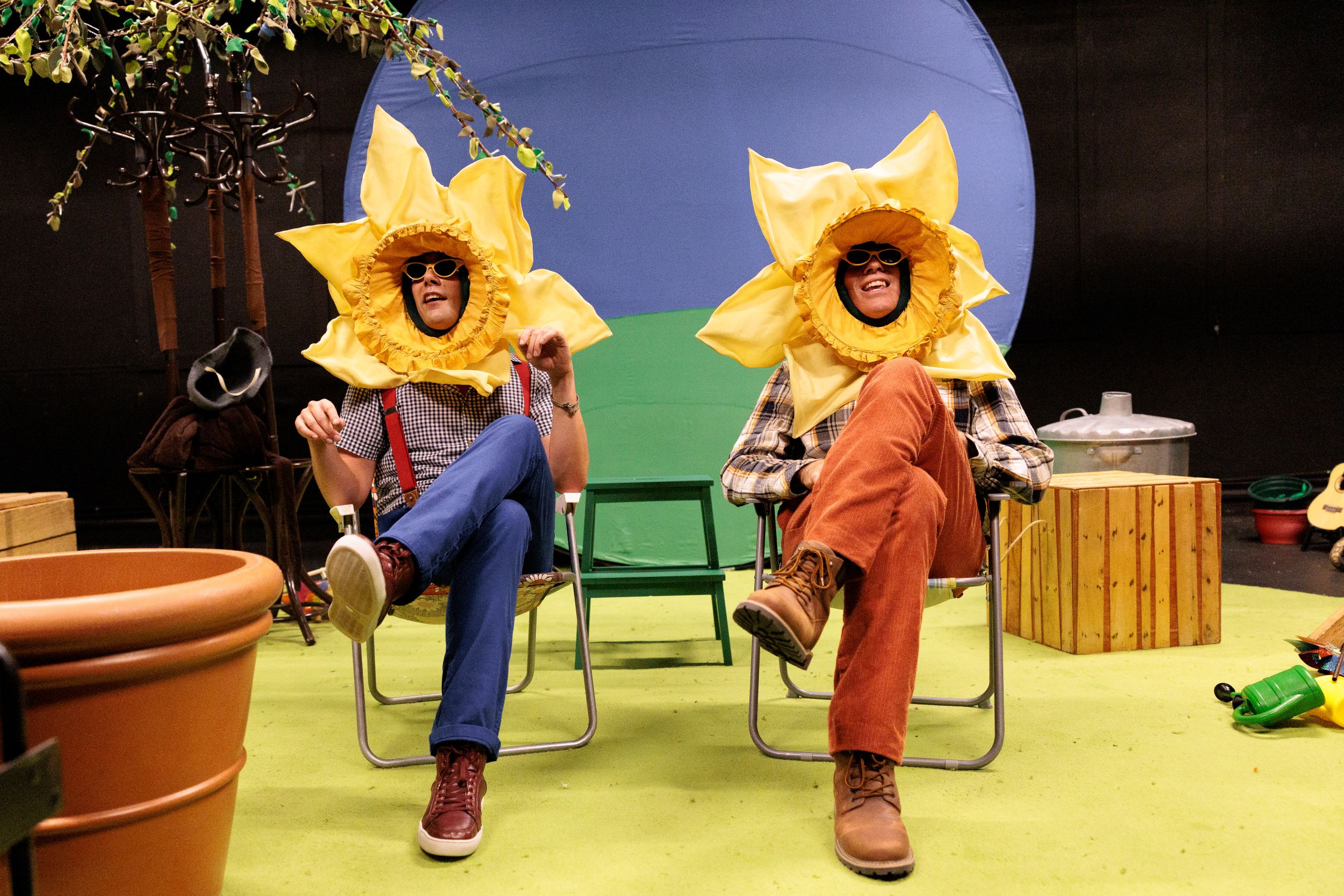 Two people in sunflower costumes sitting on lawn chairs indoors