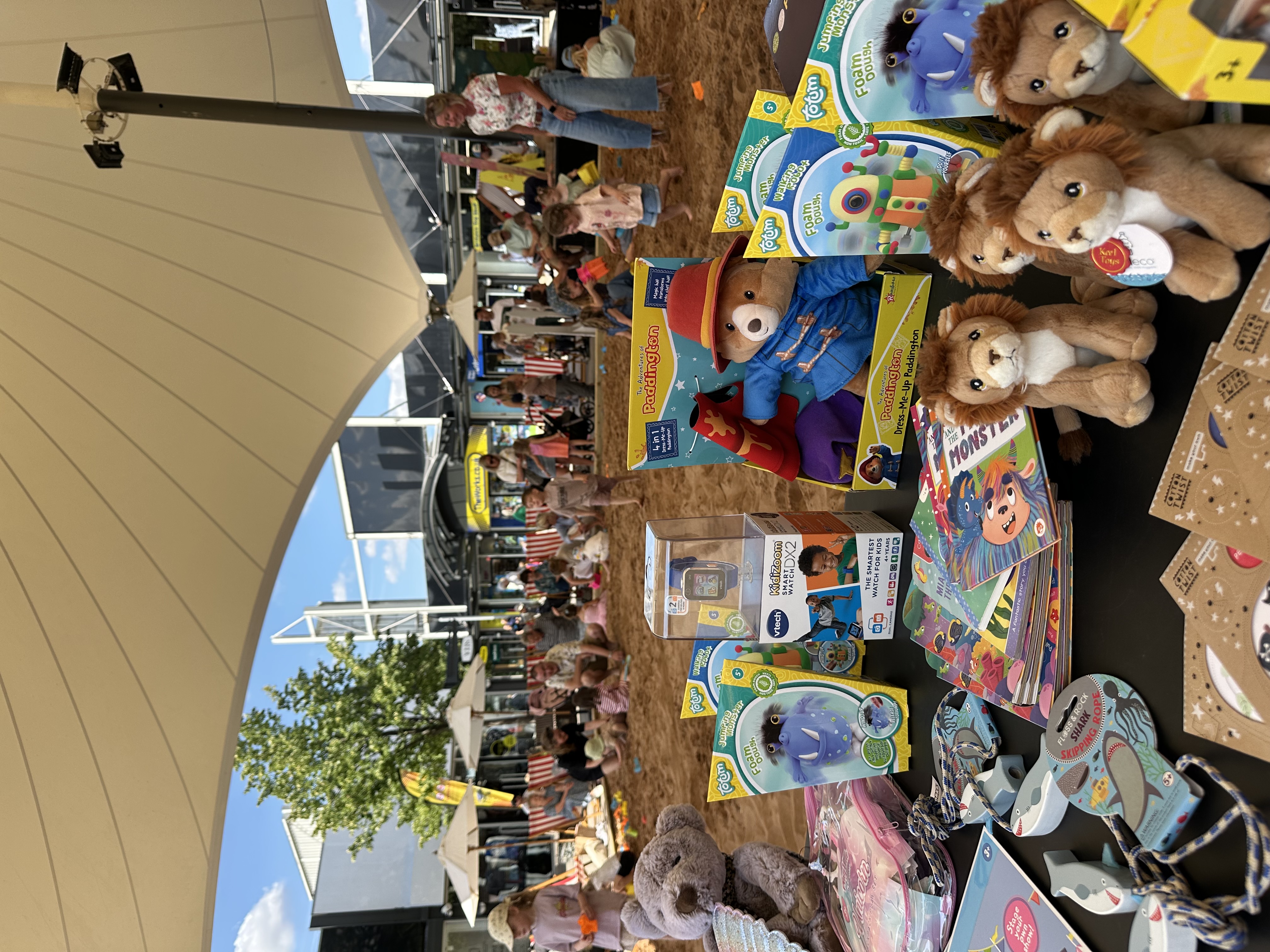 Children playing in a sandy area with toys and stalls under a canopy