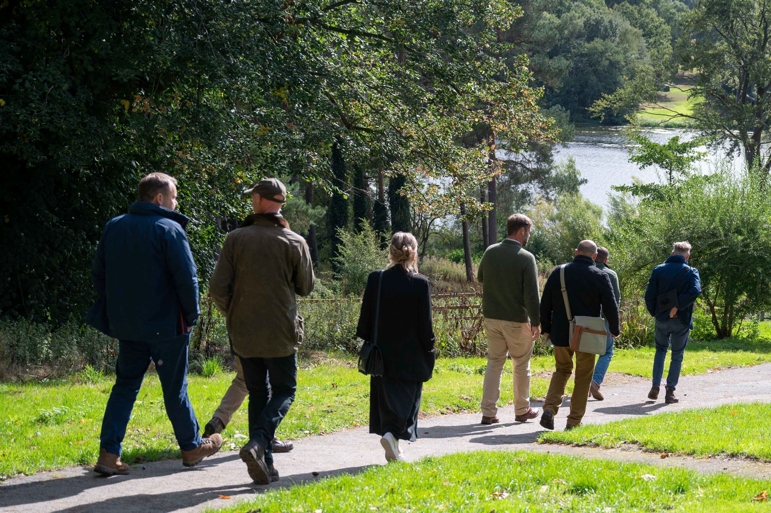 Group of people walking along a path by a lake in a park