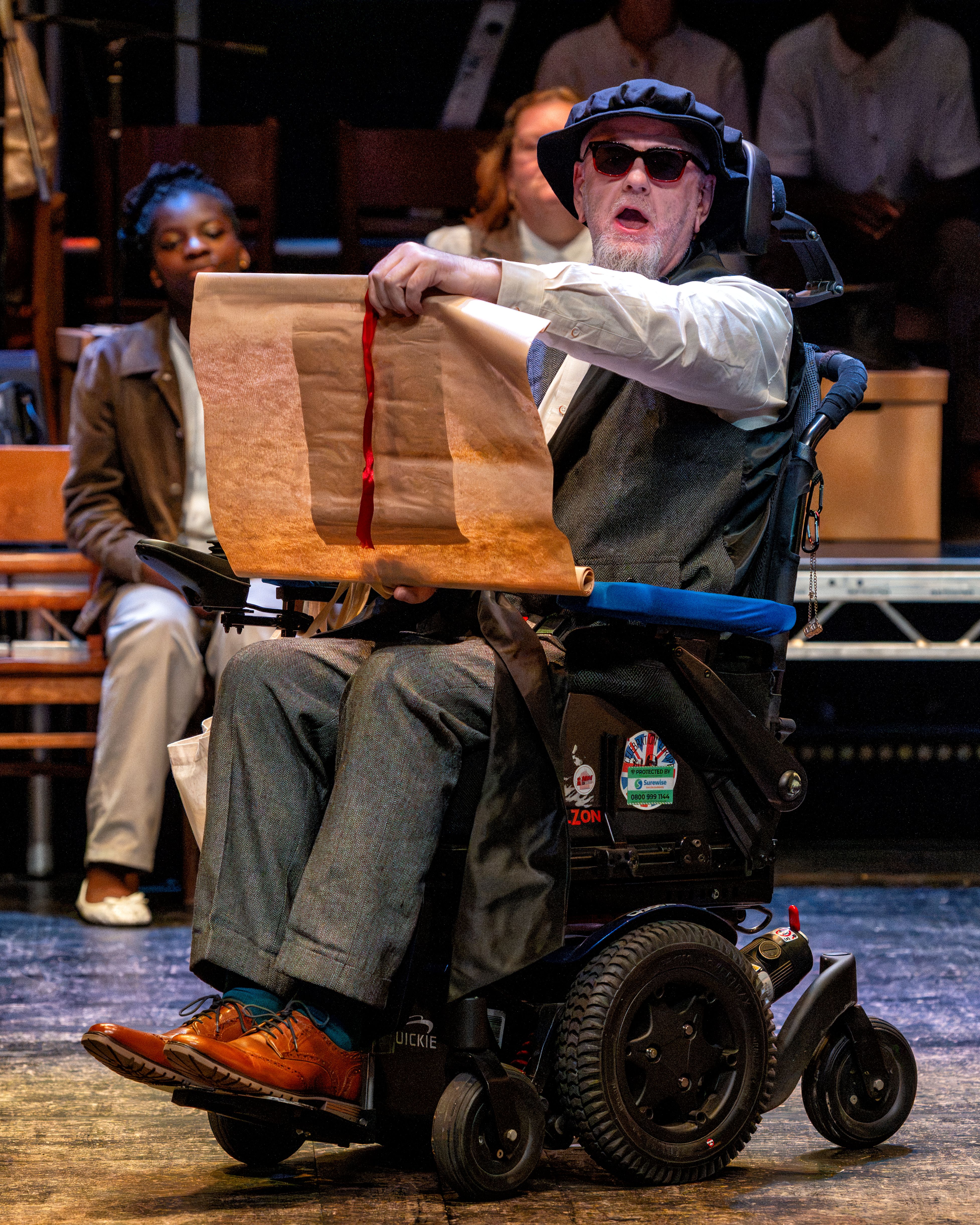 Man in a wheelchair performing on stage with a scroll