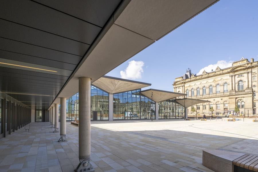 Modern glass pavilion with historic stone building in background