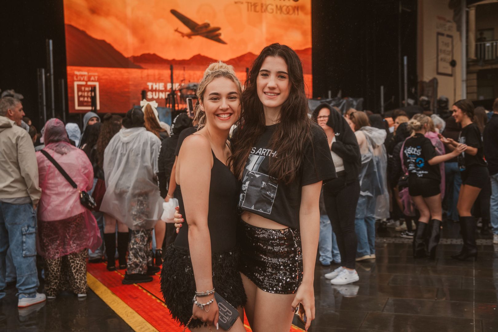 Two women smiling at outdoor concert with crowd and stage