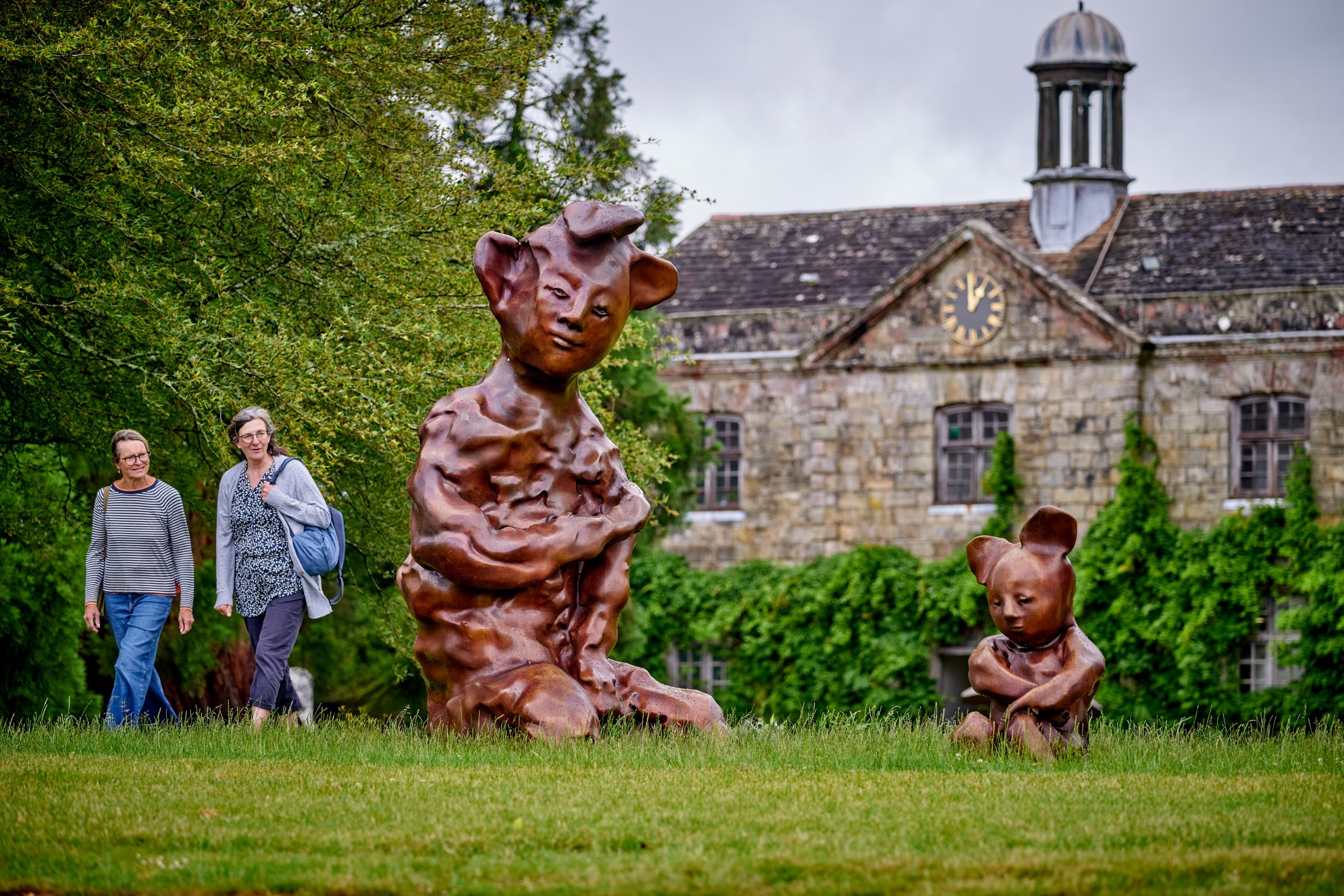 Two large whimsical bear sculptures on grass near historic building