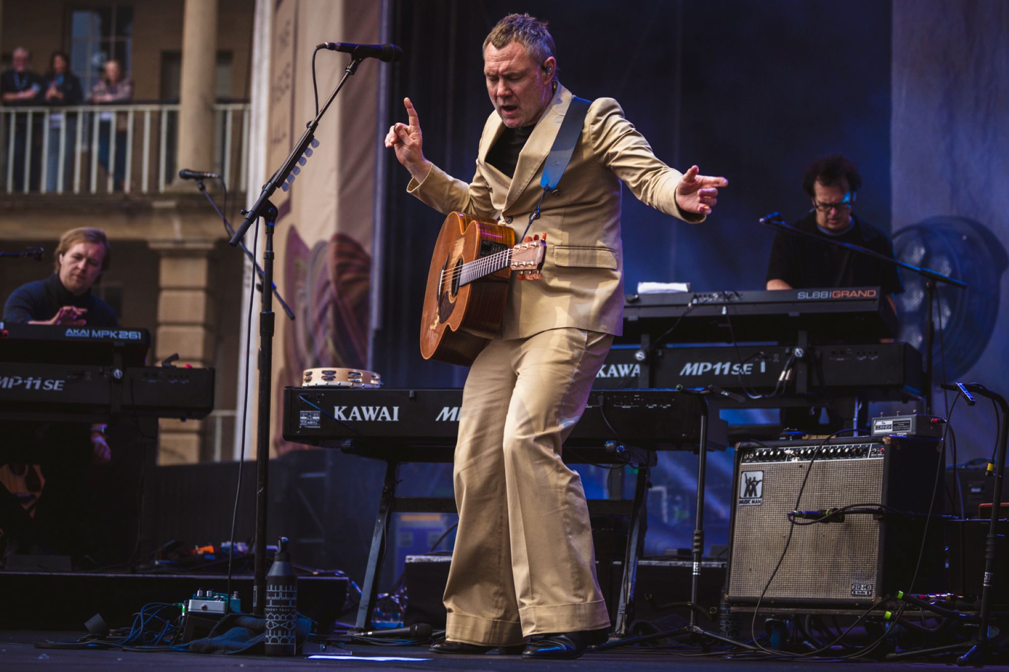 Musician in beige suit playing guitar on outdoor stage