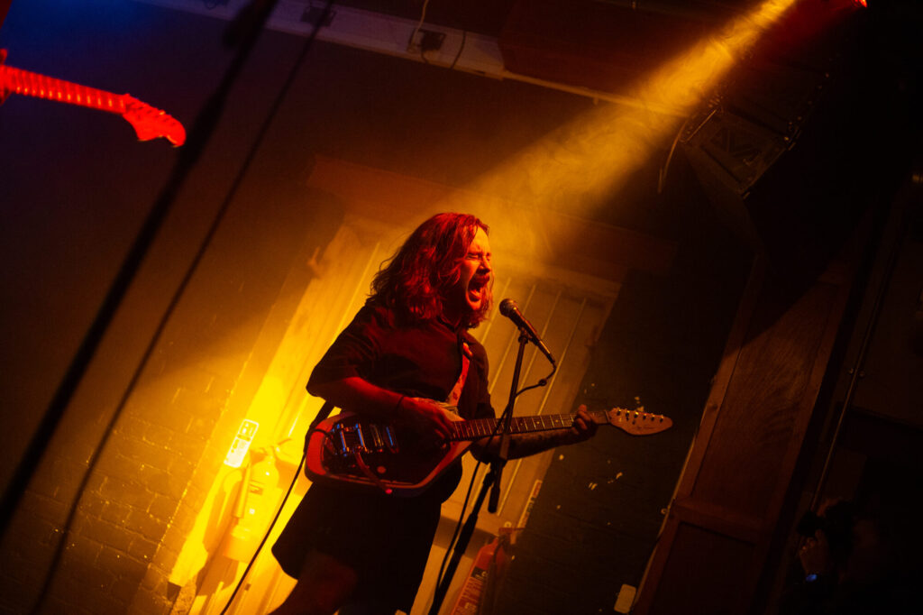 A singer passionately performs on stage with a guitar, illuminated by colorful stage lights in a vibrant venue.