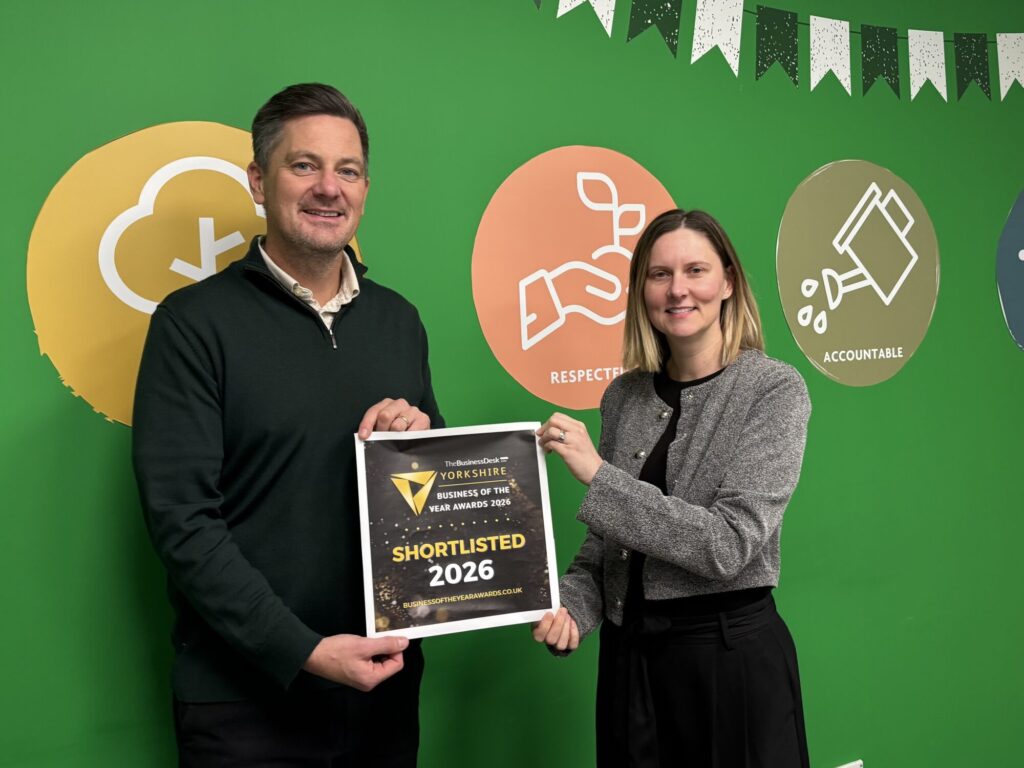 Two people stand in front of a green wall, holding an award plaque that reads