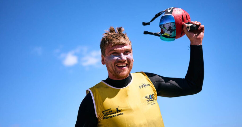 Connor Bainbridge holding his hat, in celebration. He is smiling and looking very pleased. His hair is slightly messy from wearing his protective helmet.