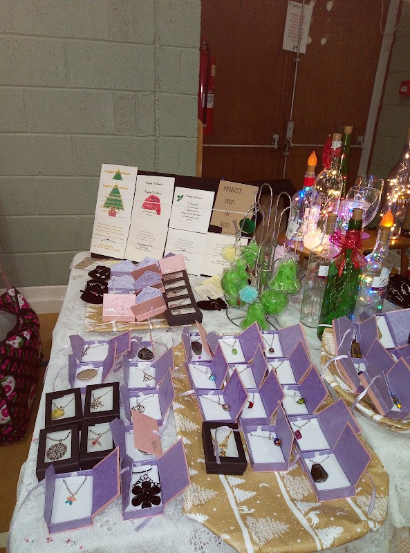 Jewelry displayed on tables with decorative items, menus, and festive decorations in a community hall setting.