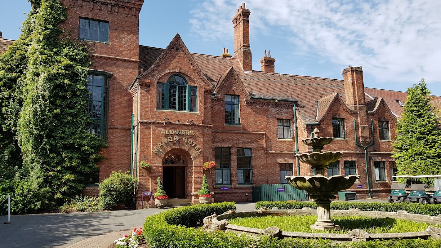 Red brick hotel facade with large windows, a fountain in front, and lush greenery surrounding the entrance.