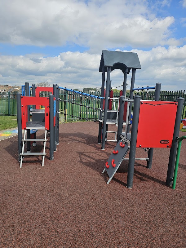 Colorful playground equipment with slides and climbing structures on a rubber surface under a partly cloudy sky.