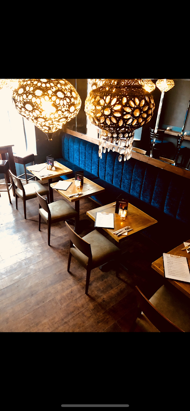Cozy restaurant interior with wooden tables, chairs, blue velvet seating, and ornate hanging lights.