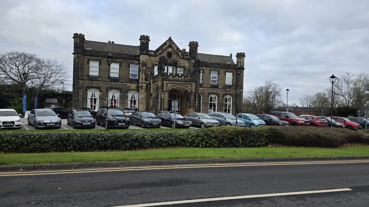 Victorian-style community hall with stone façade, large windows, and a landscaped front lawn, surrounded by parked cars.