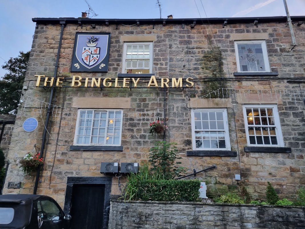 Historic stone building with "The Bingley Arms" sign, decorative plants, and blue plaque in Bardsey, Yorkshire.