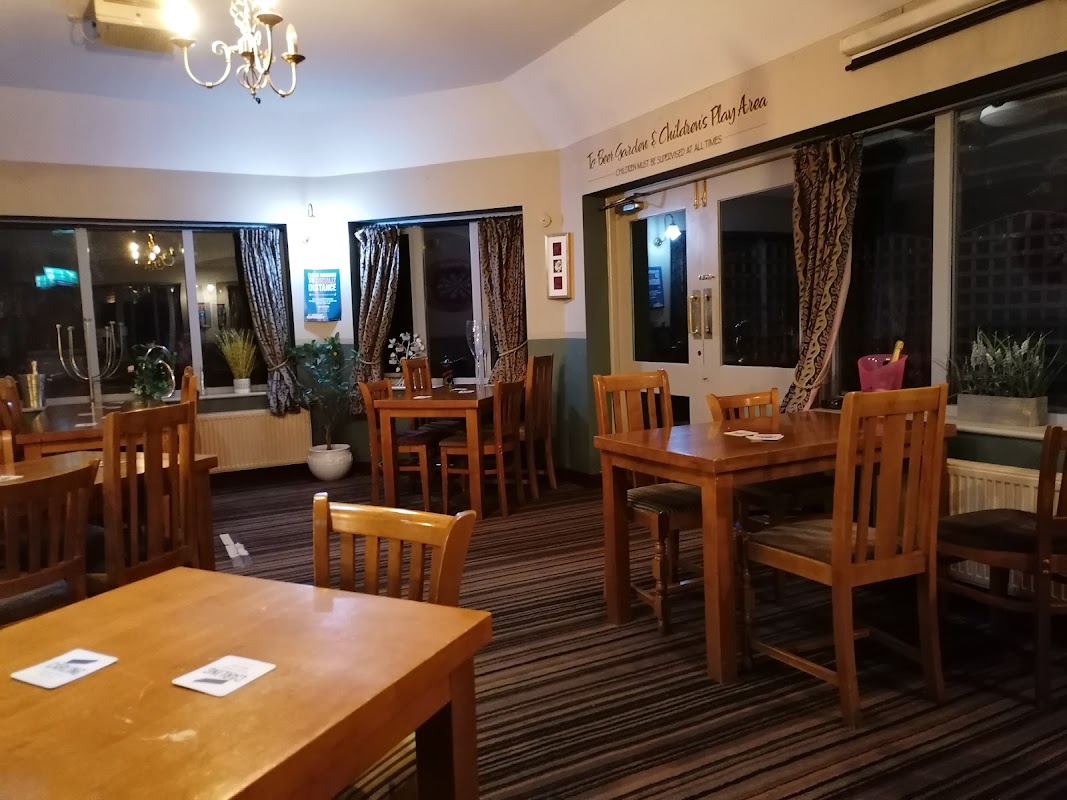 Cozy bar interior with wooden tables, chairs, patterned curtains, and potted plants in a warm, inviting atmosphere.