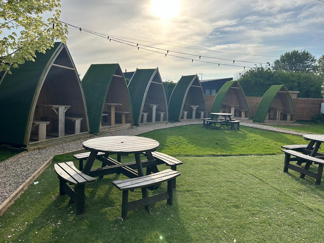 Outdoor seating area with green huts and picnic tables under a bright sky at Black Bull Retreat Bar & Restaurant.
