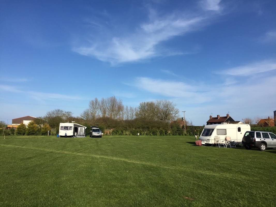 Caravans parked on green grass with trees in the background under a clear blue sky at Rectory Farm CL Caravan Site.