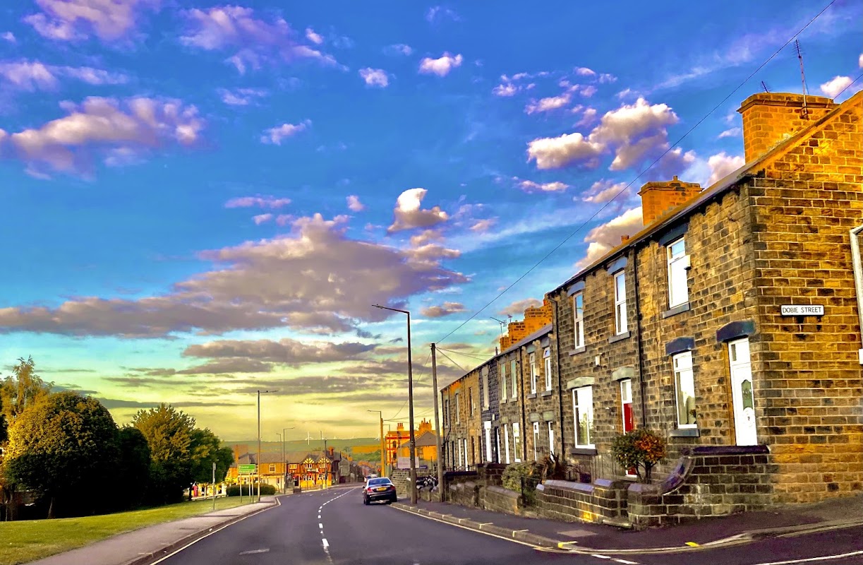 Burleigh Street West Commuter Car Park with stone houses, lush greenery, and a vibrant sky filled with clouds.