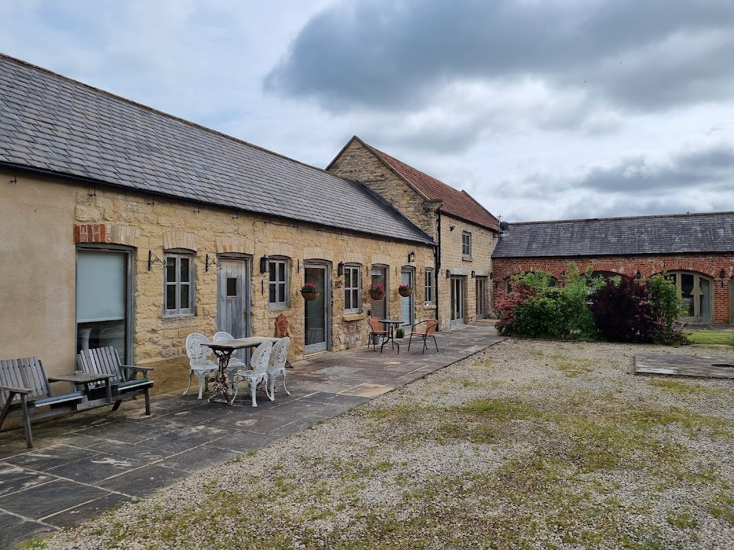 Stone cottage with outdoor seating, planters, and a gravel courtyard under a cloudy sky in Barton-le-Street, Yorkshire.