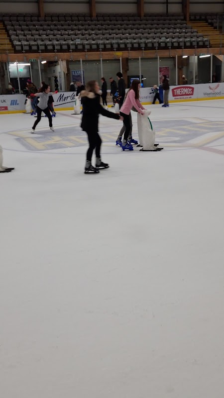 Skaters glide on ice at Elland Road's Park and Ride, with a rink backdrop and spectators in the stands.