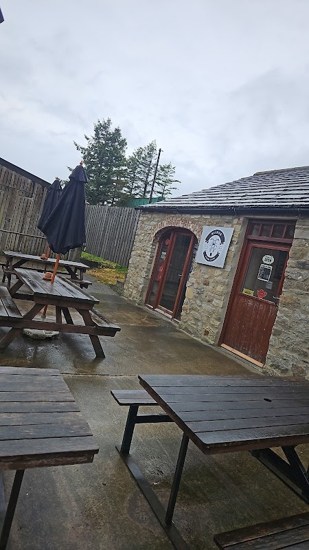 Stone building with wooden picnic tables outside, an umbrella, and a sign for "The Manor Farm Cafe" in Bellerby.