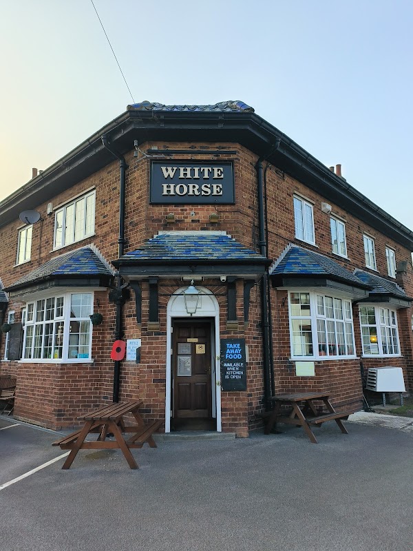 Historic brick bar with a sign reading "White Horse," featuring outdoor seating and a poppy wreath.