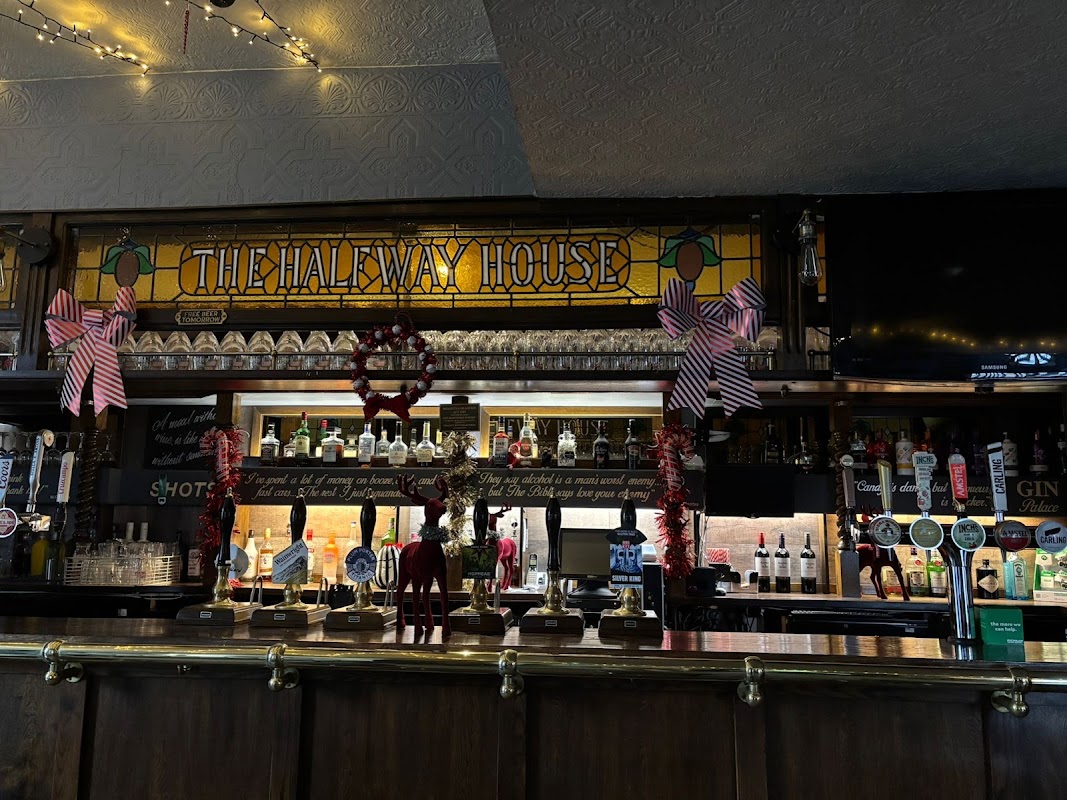 The Halfway House bar features a stained glass sign, festive decorations, and a variety of alcohol bottles on display.