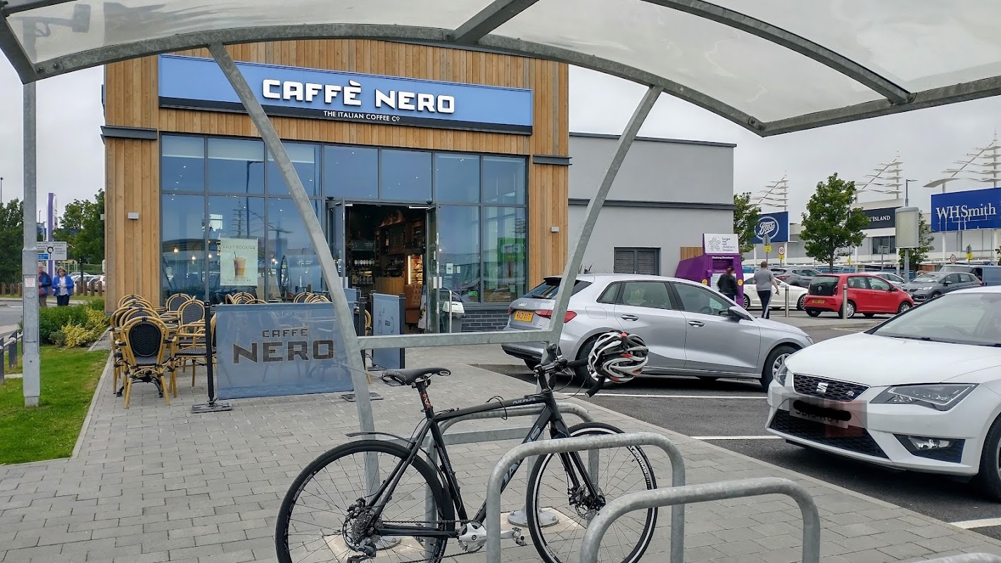Caffรจ Nero storefront at Birstall Shopping Park, with a bicycle parked in front and cars in the parking lot.