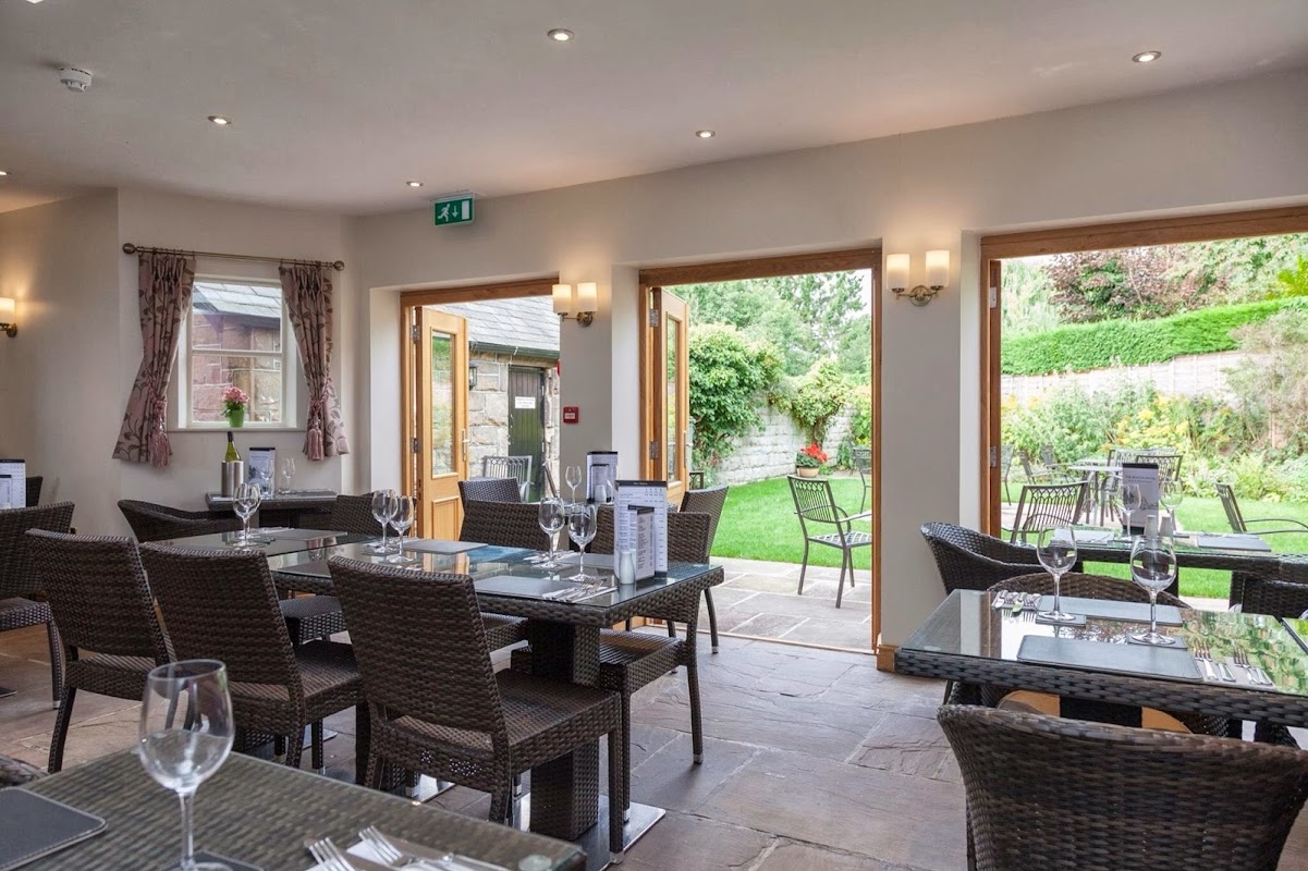Cozy bar interior with tables set for dining, large windows opening to a lush garden area.