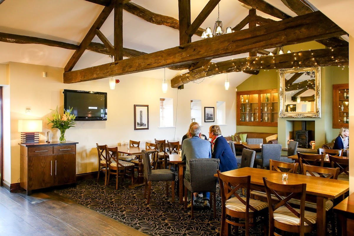 Cozy bar interior with wooden beams, tables, chairs, and a TV; patrons enjoying drinks in a warm atmosphere.