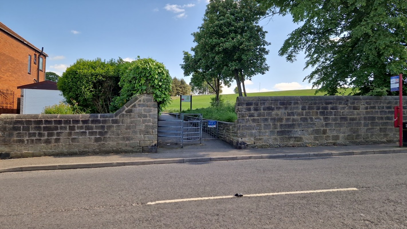 Pedestrian entrance to Bramley Park with stone walls, a gate, and greenery, set against a clear blue sky.