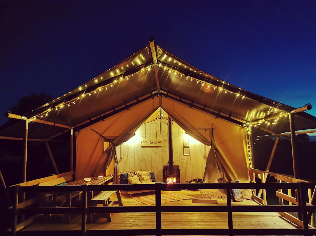 Cozy glamping tent illuminated with fairy lights, wooden deck, and peaceful evening sky at Kingfisher Lakes, Yorkshire.