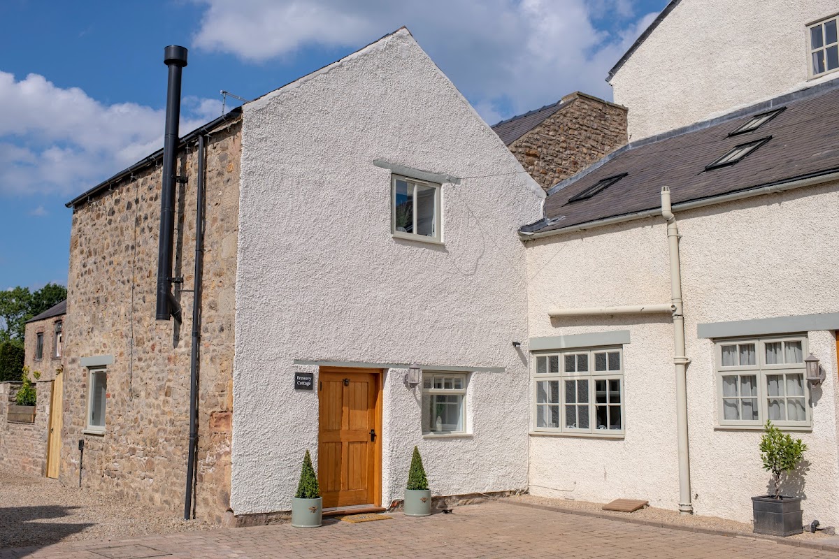Brewery Cottage features a mix of stone and white-rendered walls, a wooden door, and potted plants by the entrance.