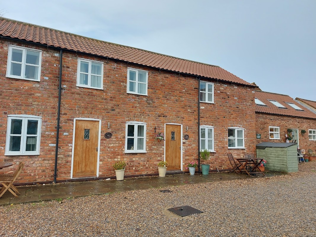 Charming brick cottages with wooden doors, potted plants, and outdoor seating in a tranquil rural setting.