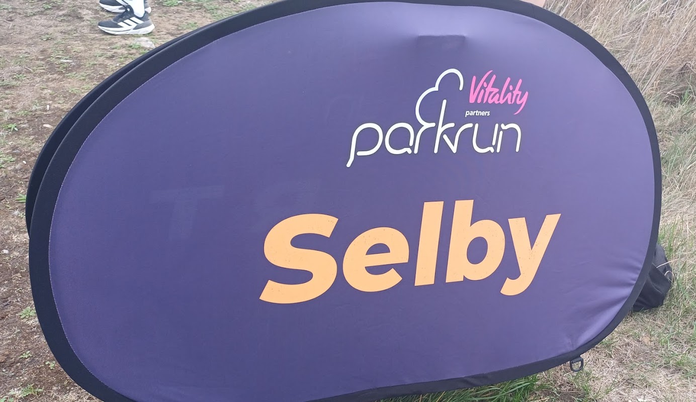 Purple banner displaying "Selby" and "parkrun" logos, set against a grassy area.