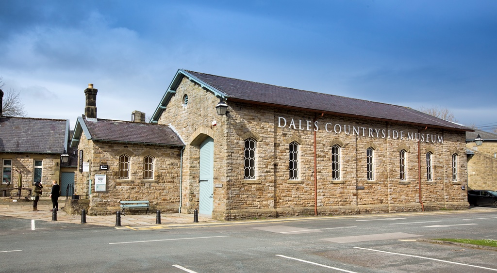 Historic stone building with large windows, sign reading "Dales Countryside Museum," and a person standing nearby.