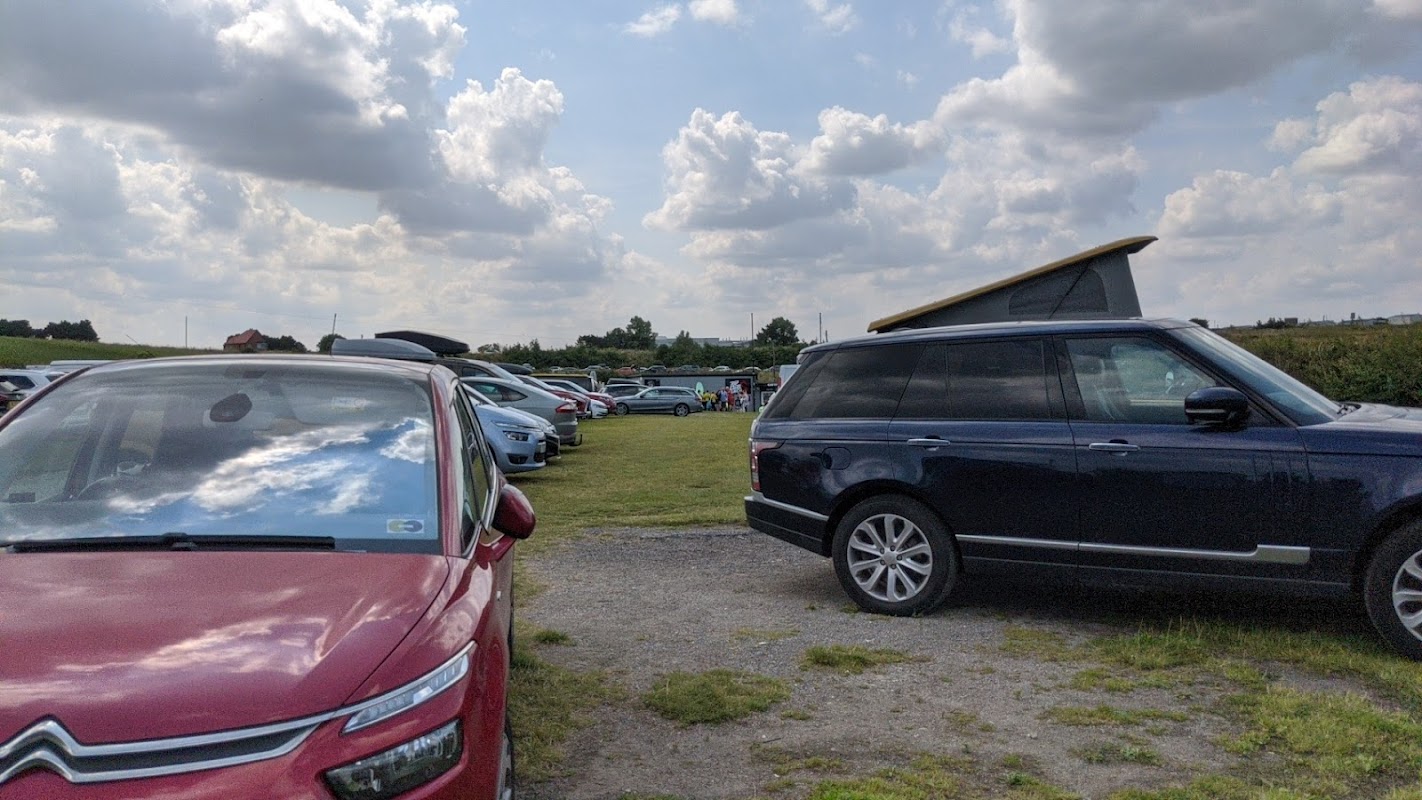 Busy car park at Cayton Bay Beach with various vehicles and a grassy area under a partly cloudy sky.