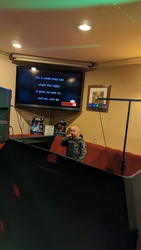 A small stage with a microphone, a karaoke screen displaying lyrics, and colorful lights in a lively atmosphere.