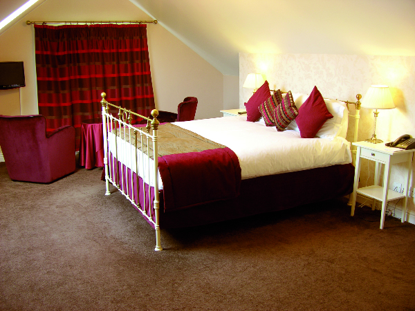 Elegant hotel room with a brass bed, red accents, and cozy armchairs, set in Cliffemount Hotel, Runswick Bay.