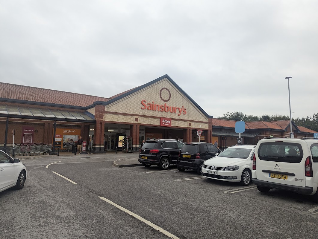 Sainsbury's store front with Argos, parked cars, and cloudy sky in Colton, Yorkshire.