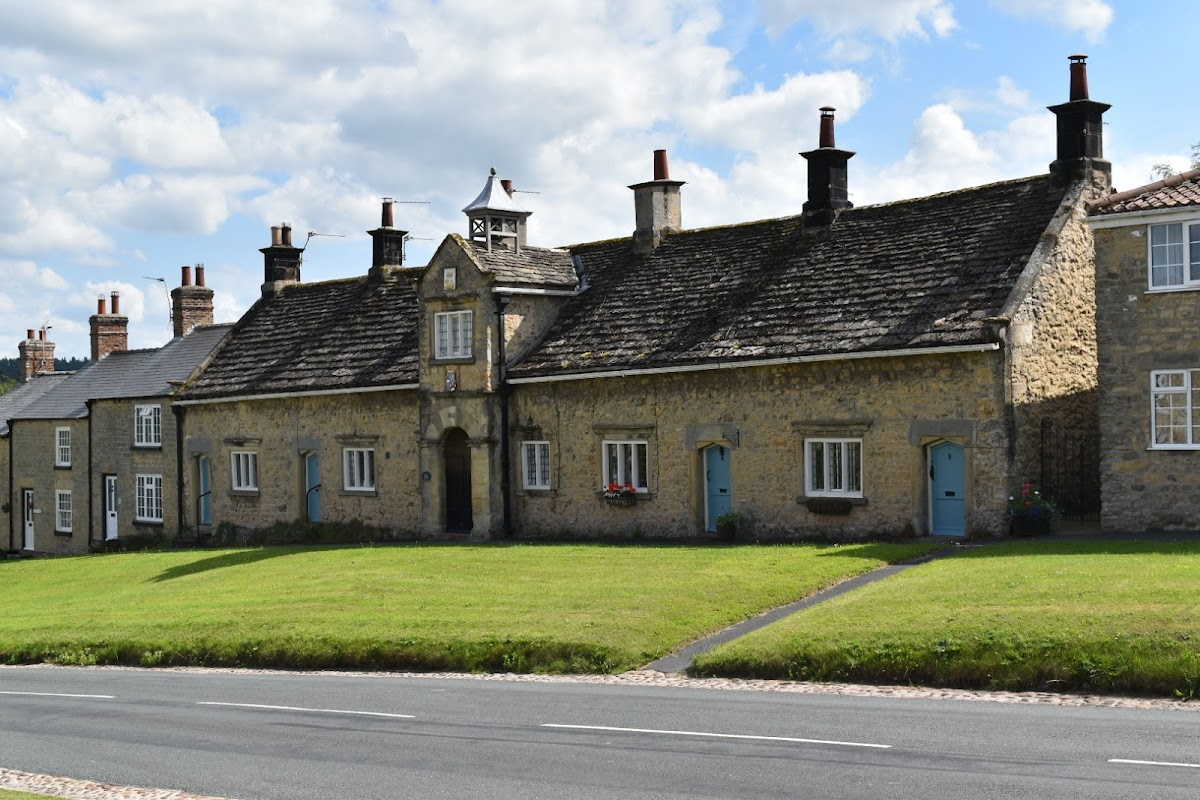 Coxwold Village Hall features a stone façade with a central entrance and a clock tower, surrounded by green grass.